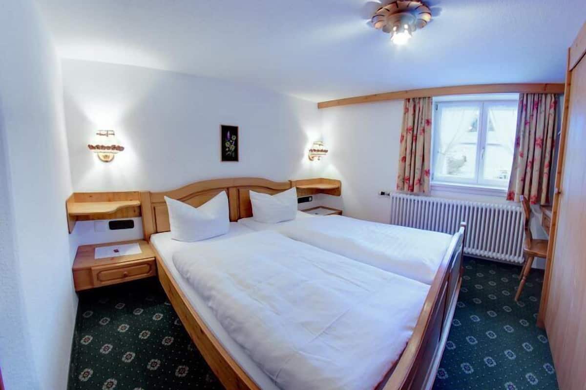 Habitación de hotel con una cama grande, cabecera de madera, mesitas de noche y una ventana con cortinas.