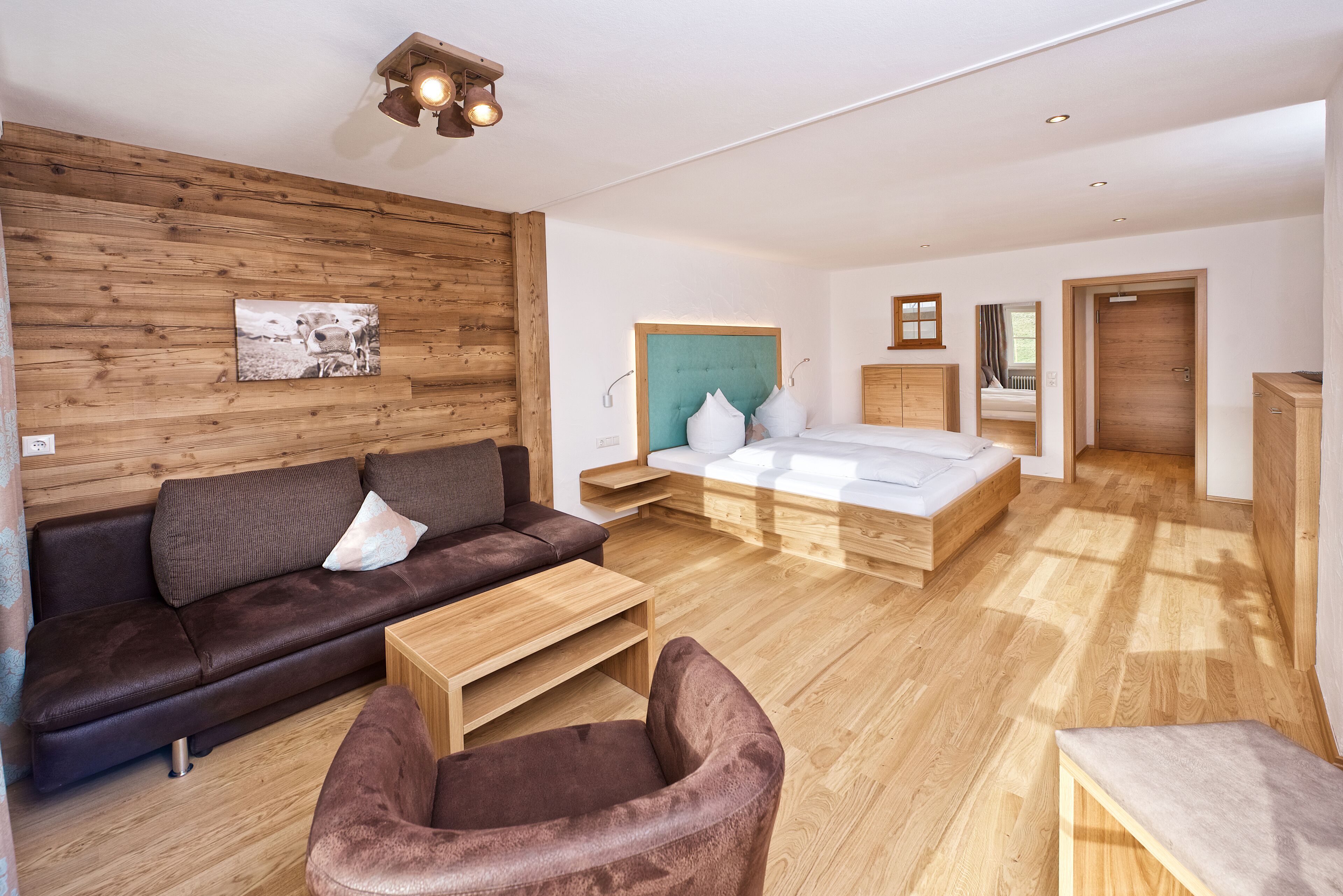 A modern living room with a sofa, armchair, and a bed with a wooden headboard.