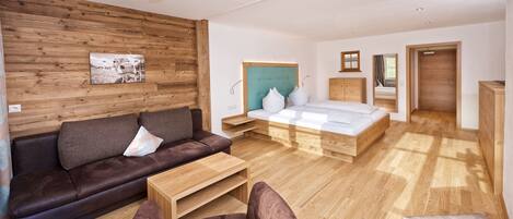 A modern living room with a sofa, armchair, and a bed with a wooden headboard.