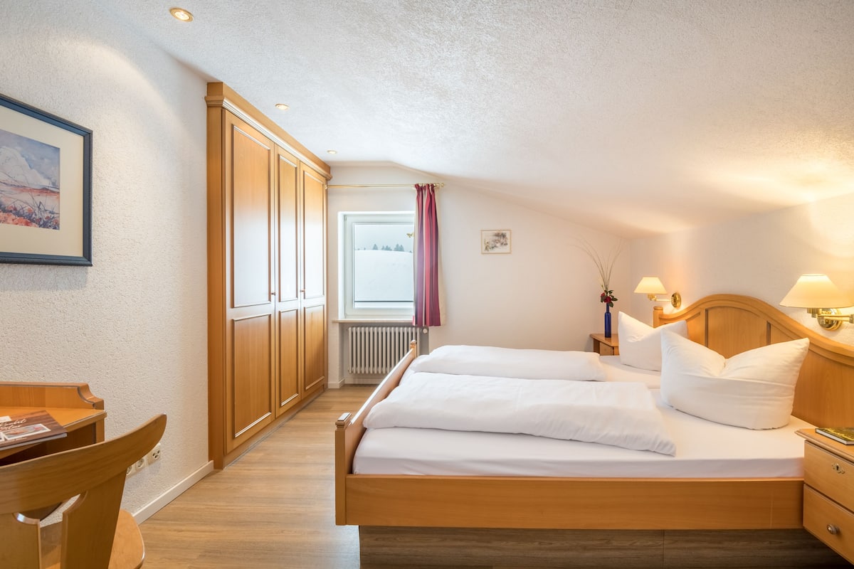 Un dormitorio con una cama de madera, un escritorio y un ventanal con cortinas.