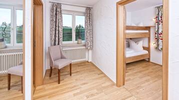 A room with a wooden floor, a chair, a window with curtains, and a bunk bed with pillows.