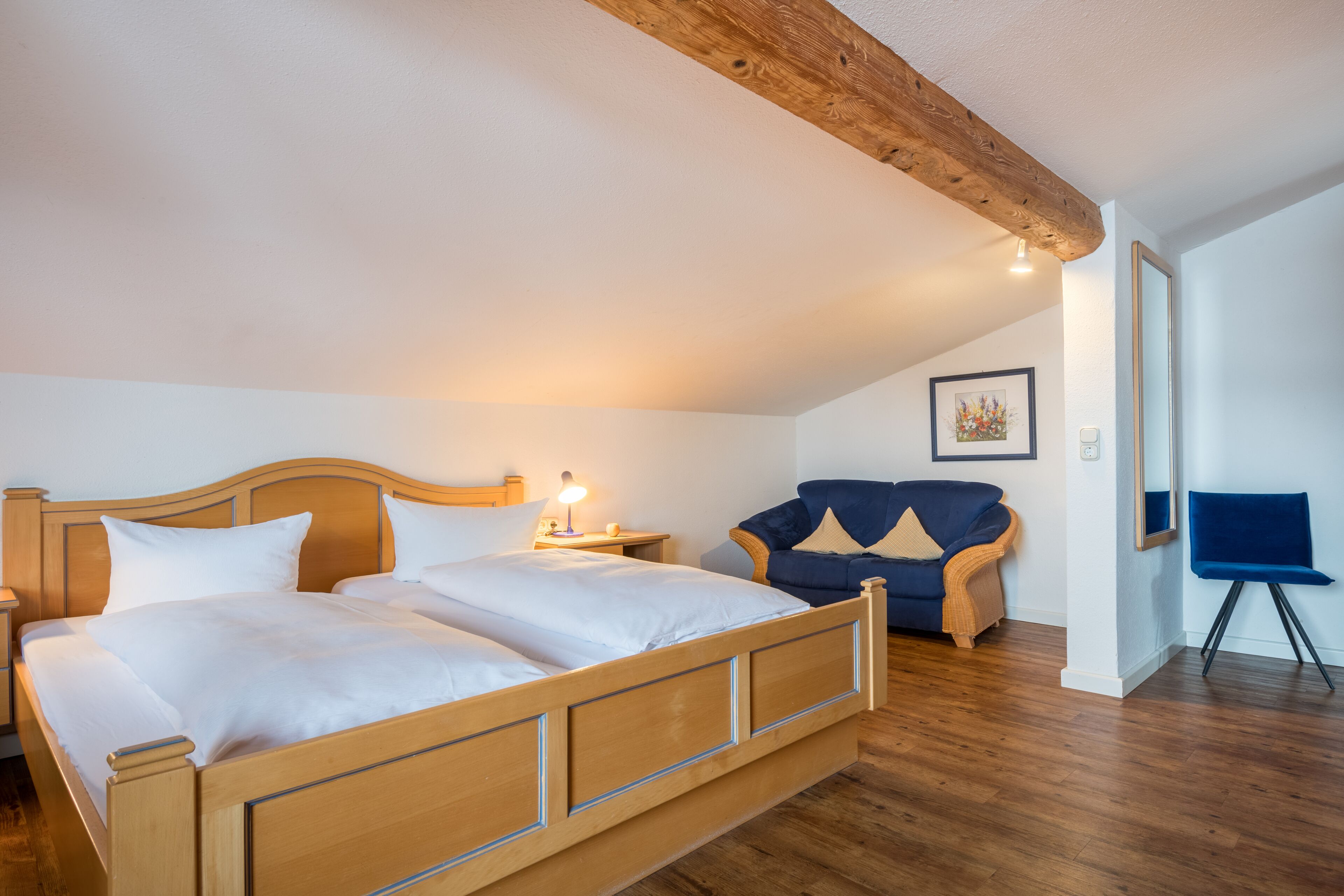 Un dormitorio con una cama de madera, una mesita de noche, un sillón azul y un espejo.