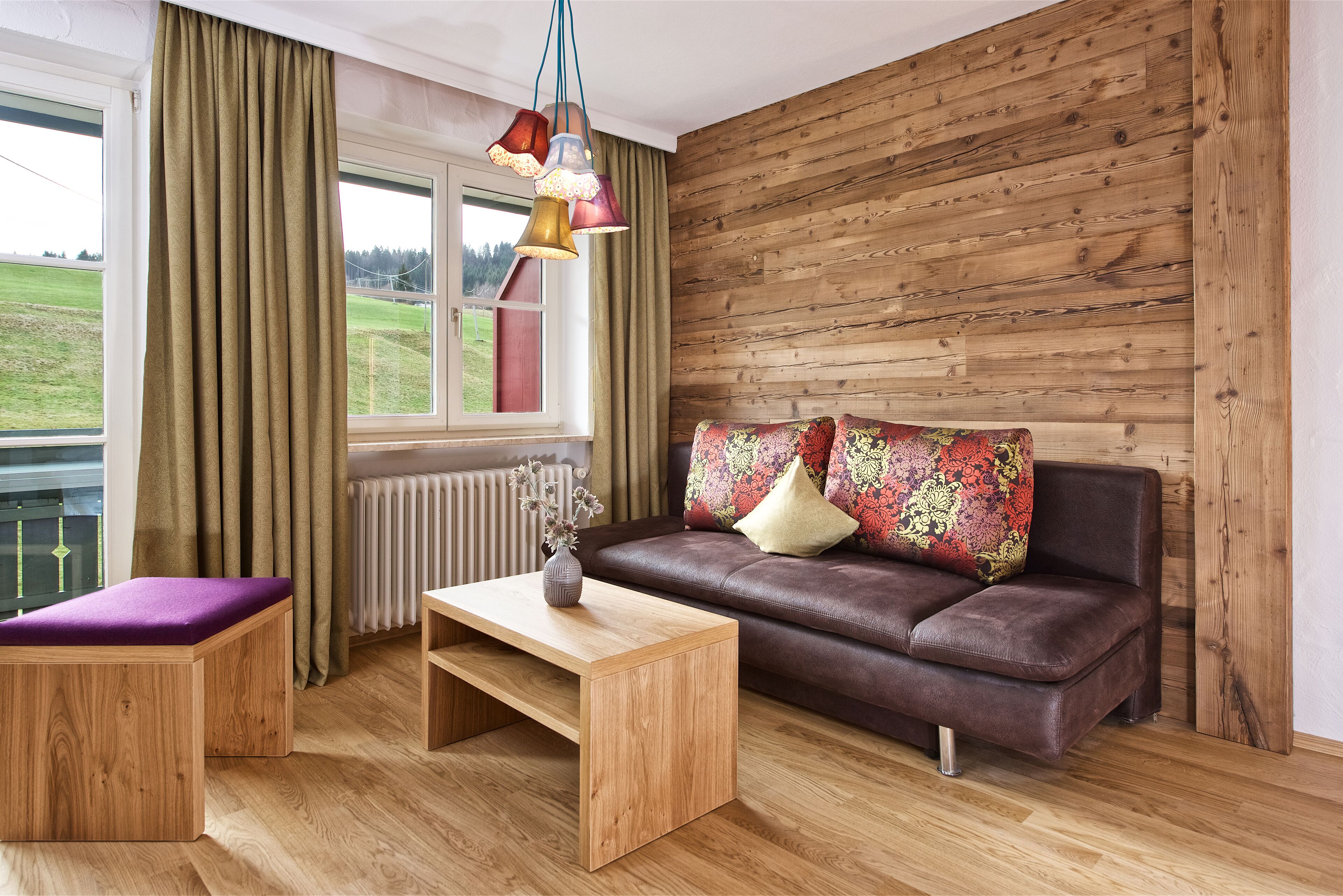 A cozy living room with a brown leather sofa, a wooden coffee table, a purple cushioned bench, and a window with curtains.