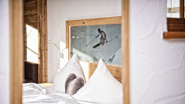 Una cama con ropa de cama y almohadas blancas, un cuadro enmarcado de un esquiador y un cabecero de madera.