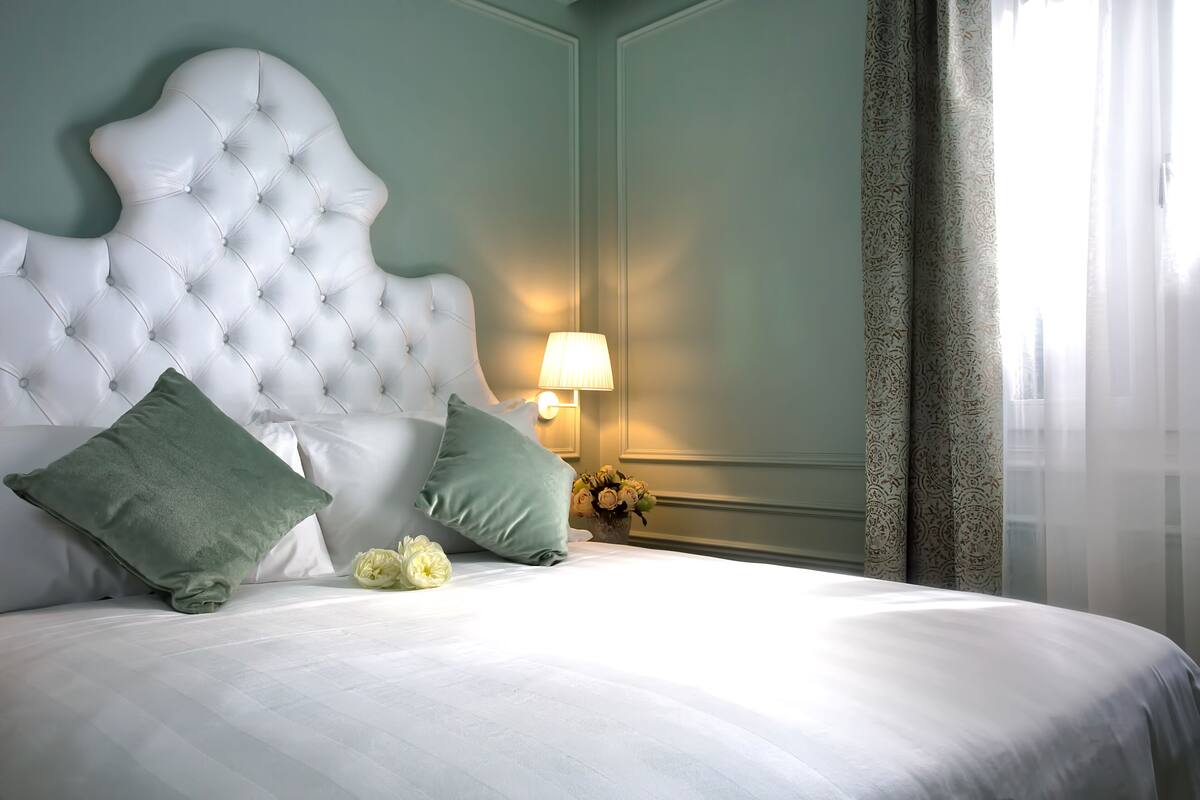A neatly made bed with a tufted headboard, two pillows, and a vase of flowers.