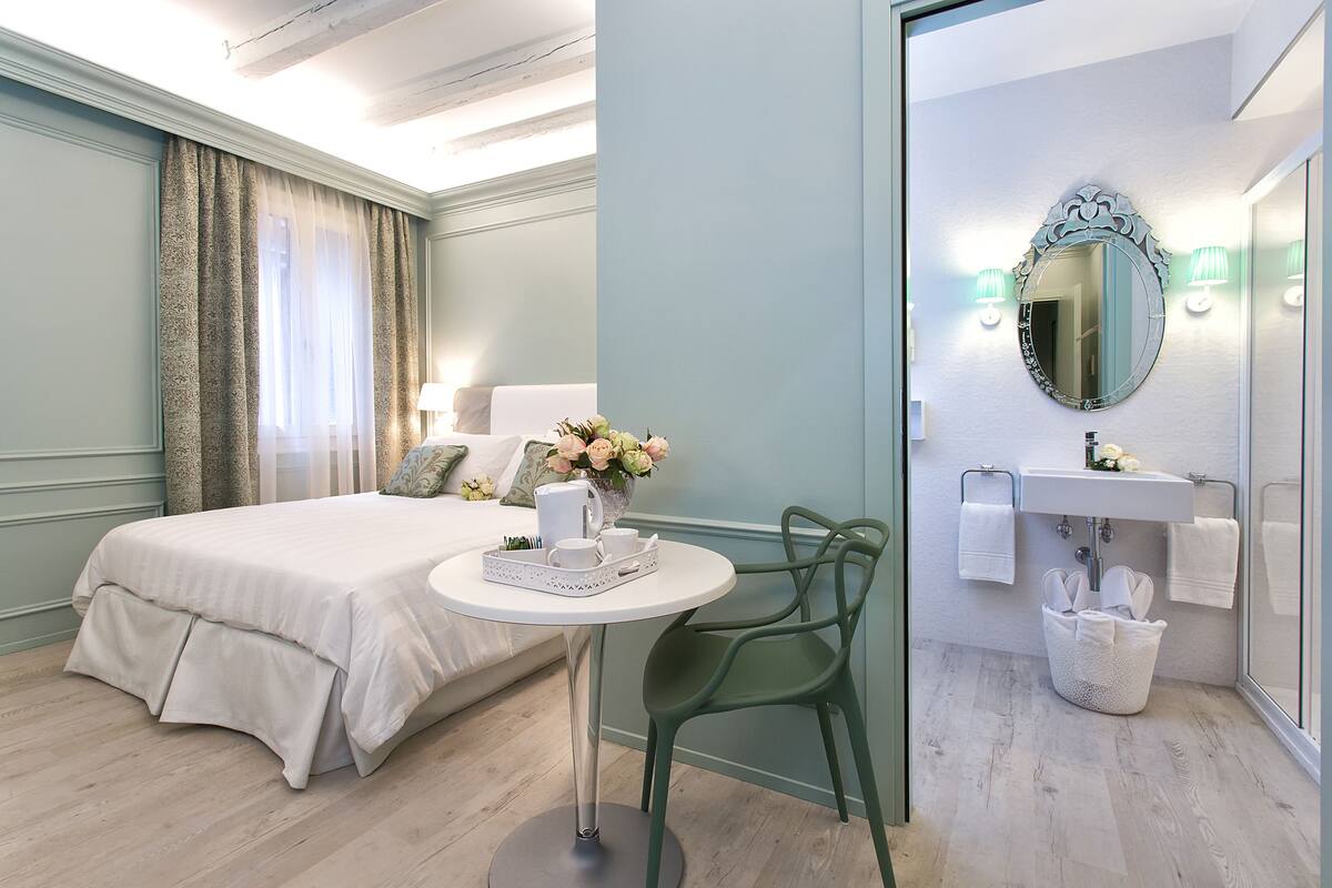 A hotel room with a bed, a round table with a tray, a chair, a sink, and a mirror.