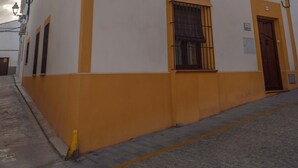 A two-story building with a yellow and white facade, multiple windows with metal bars, and a visible door. - Andalusian village family house (Peñaflor)