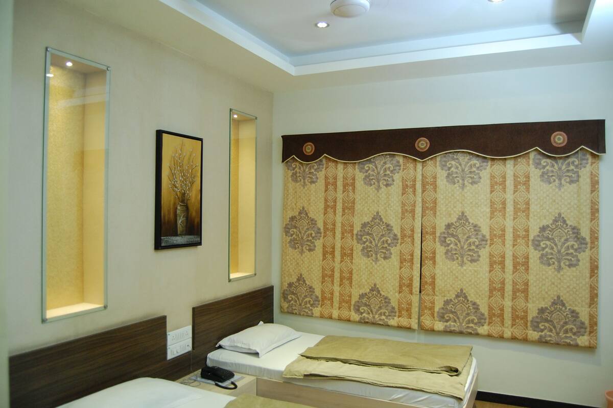 Habitación de hotel con cama, mesita de noche, espejo y cortina decorativa.