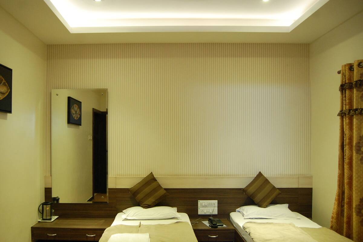 Una habitación de hotel con dos camas, una mesita de noche con lámpara, un espejo y un cuadro en la pared.