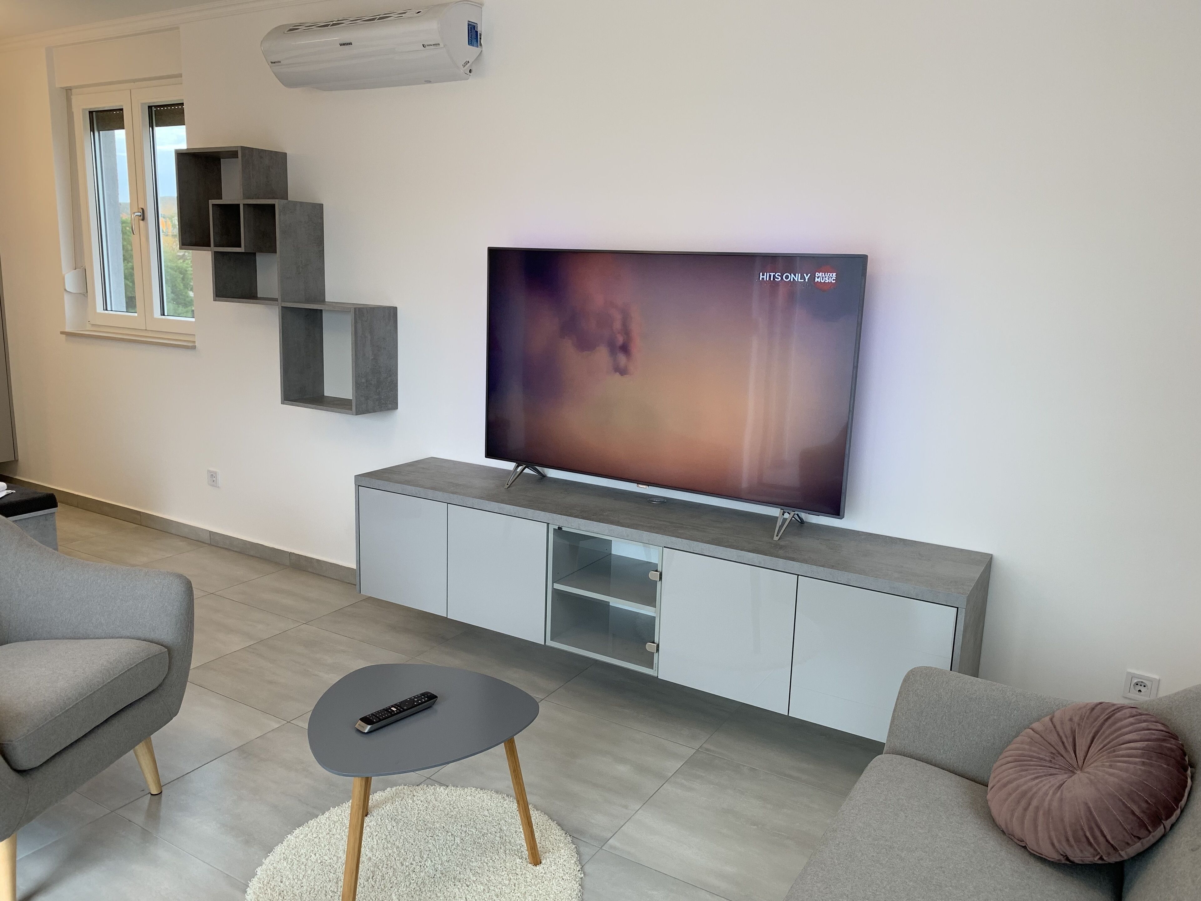 A modern living room with a flat-screen TV, grey sofas, a coffee table, and built-in shelving.