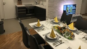 Eine moderne Küche mit weißen Schränken, einem eingebauten Ofen und einem Essbereich, der für eine Mahlzeit gedeckt ist, mit einem Fernseher, der eine Bierwerbung zeigt.