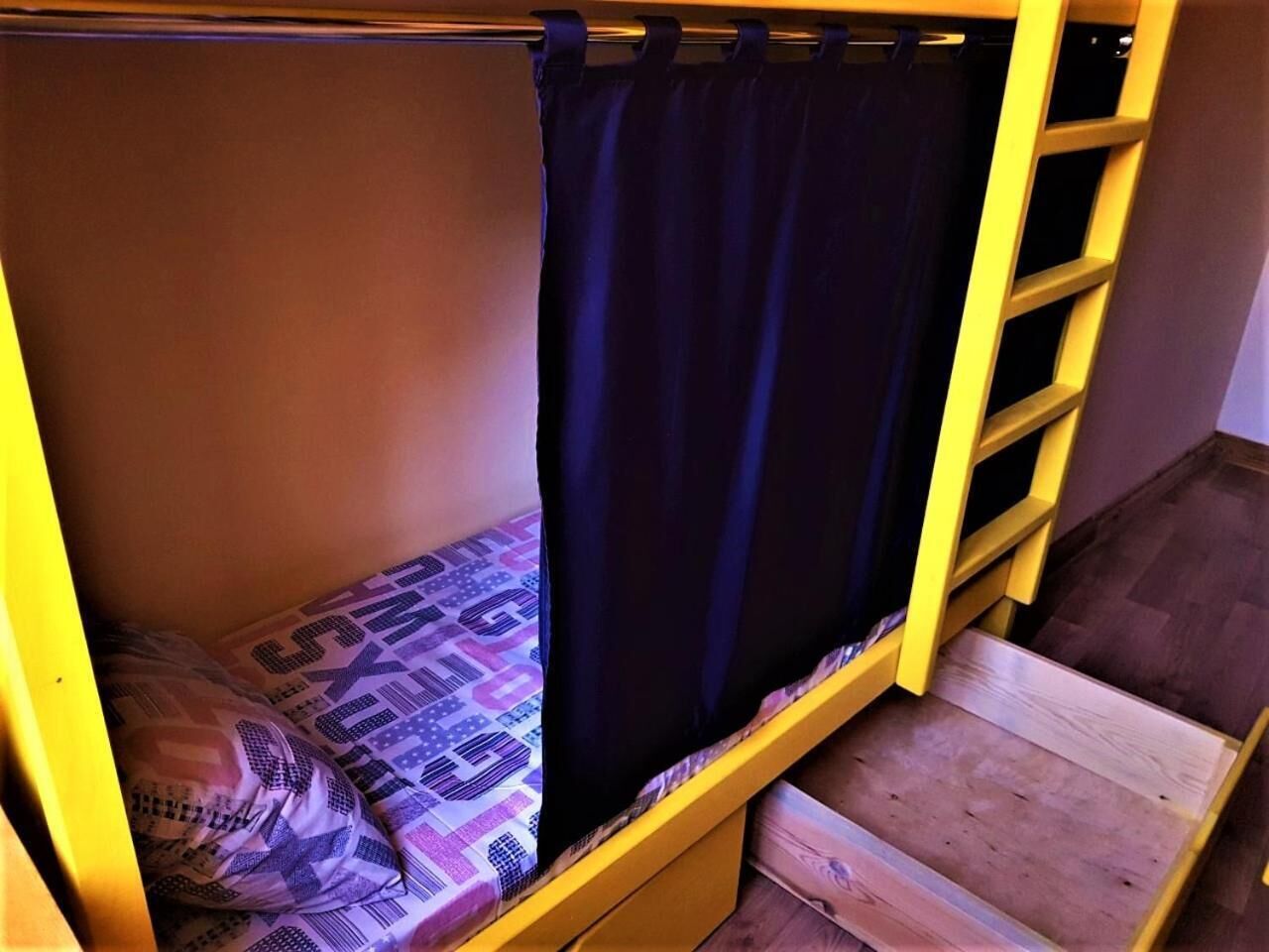 A bunk bed with a patterned bedspread, a dark curtain, and a wooden ladder.