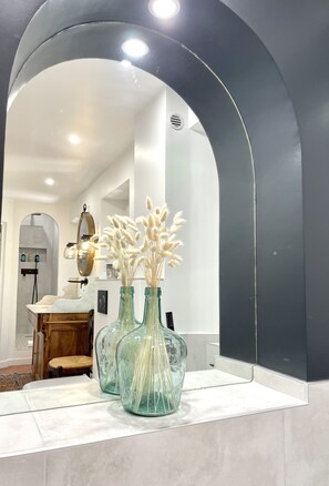 A bathroom vanity with two glass vases containing dried pampas grass, a mirror, and a wooden chair. - Château de Saint-Girons Luxury Guest House in Provence (Aix-en-Provence)