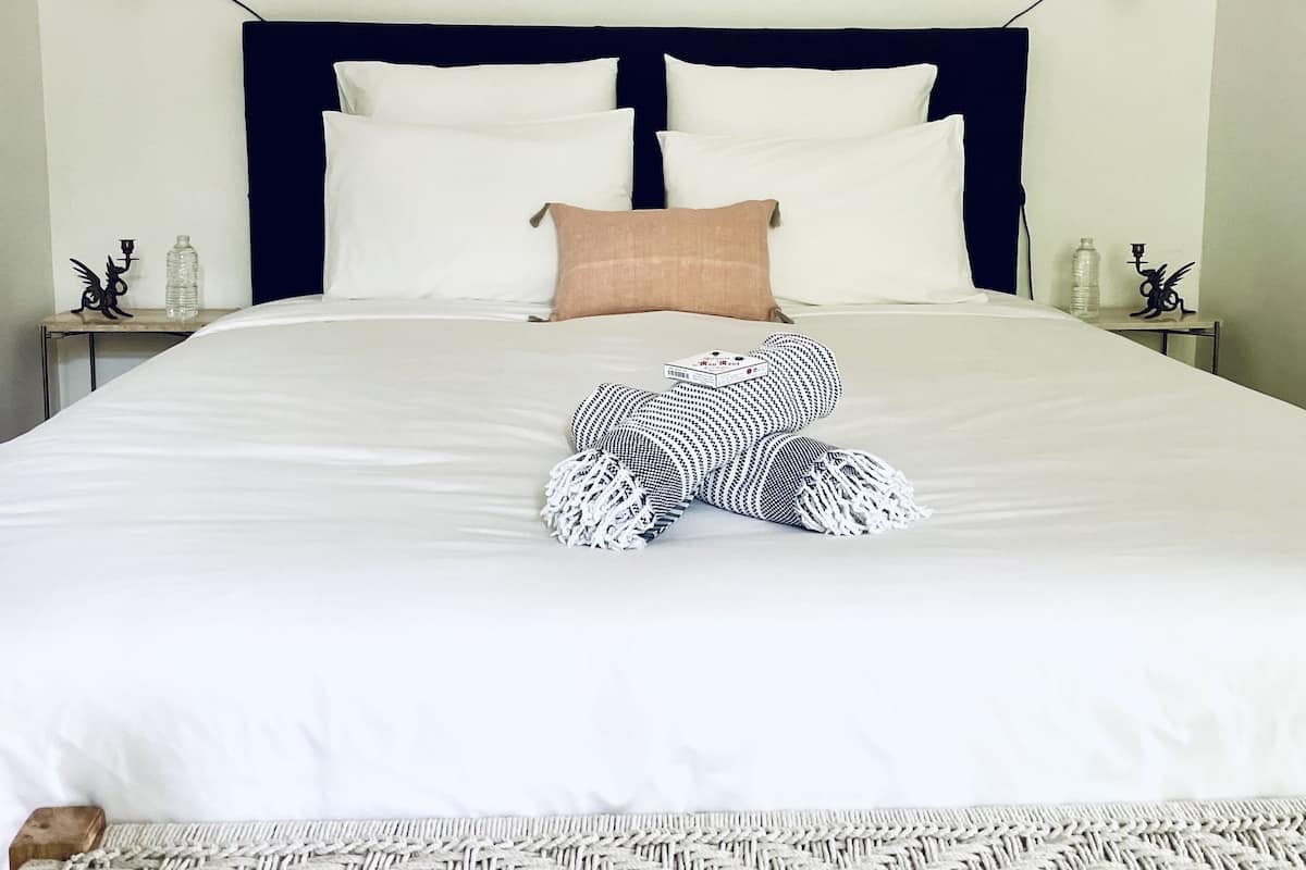 Un lit bien fait, avec du linge de lit blanc, une tête de lit sombre et un coussin décoratif.