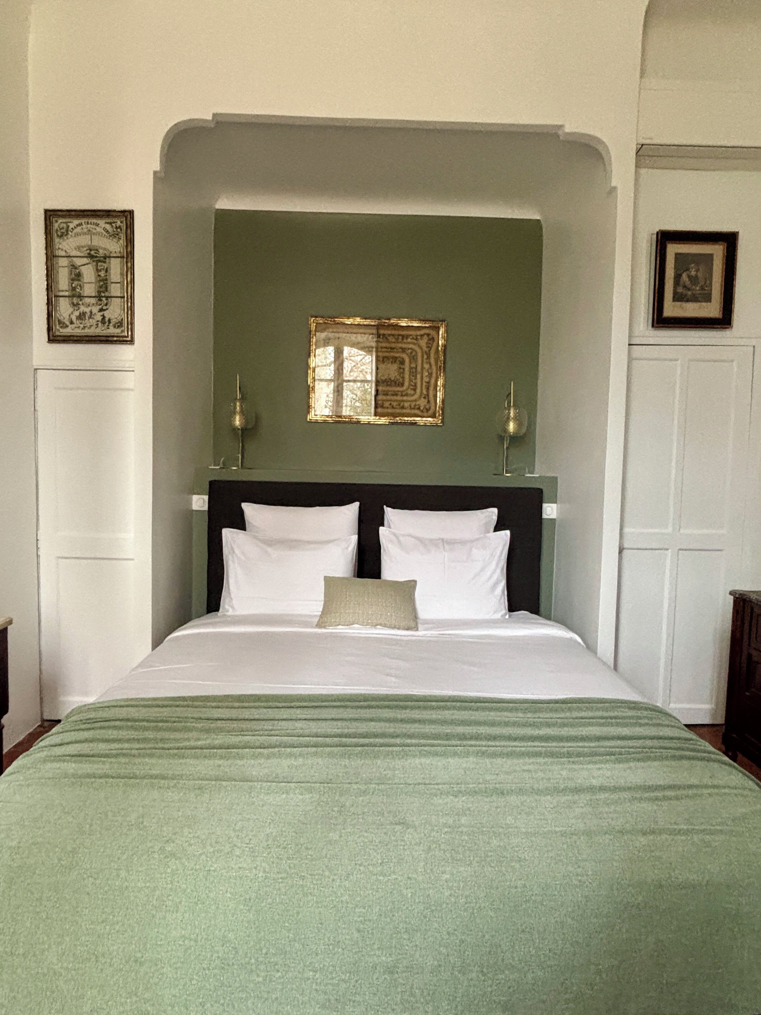 A neatly made bed with white linens and a green throw blanket, a dark headboard, and two wall-mounted lamps.