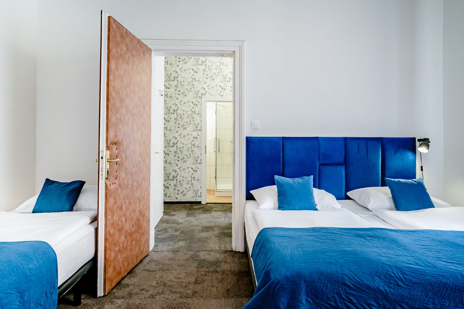 A hotel room with two beds, a wooden door, and a bathroom visible through an open door.