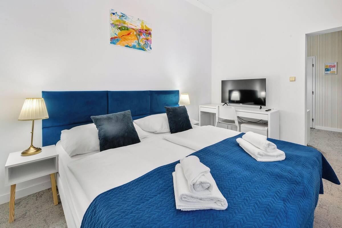 A hotel room with a large bed, a desk with a television, and a painting on the wall.