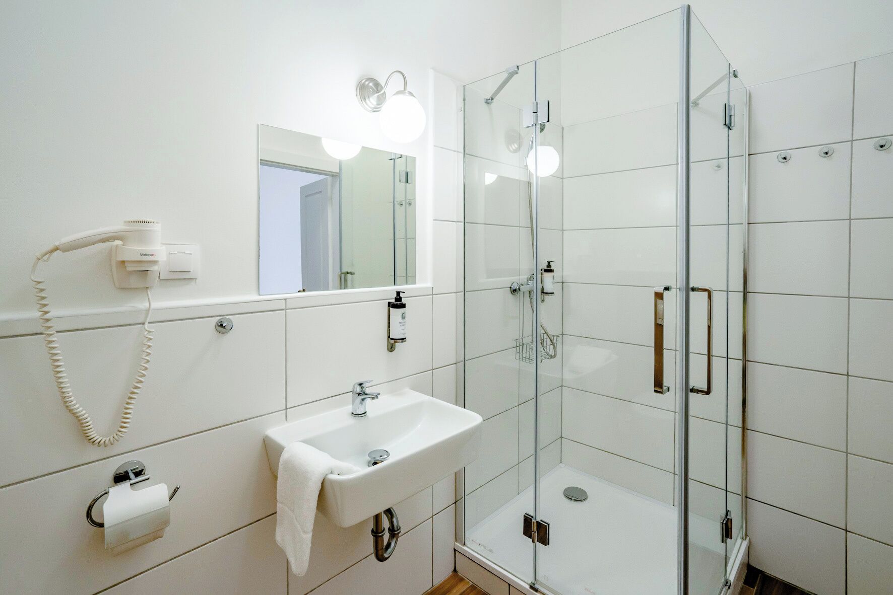 Une salle de bain moderne avec une douche à parois de verre, un lavabo blanc, un miroir et un sèche-cheveux.