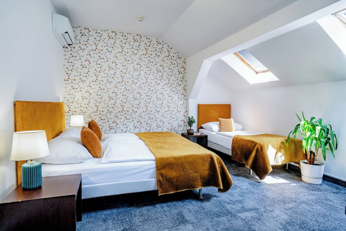 A hotel room with two beds, a skylight, a potted plant, and a patterned wall.
