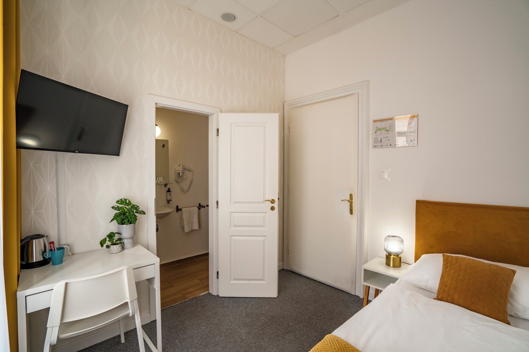 Habitación de hotel con escritorio, cama, televisión y baño visible a través de una puerta abierta.