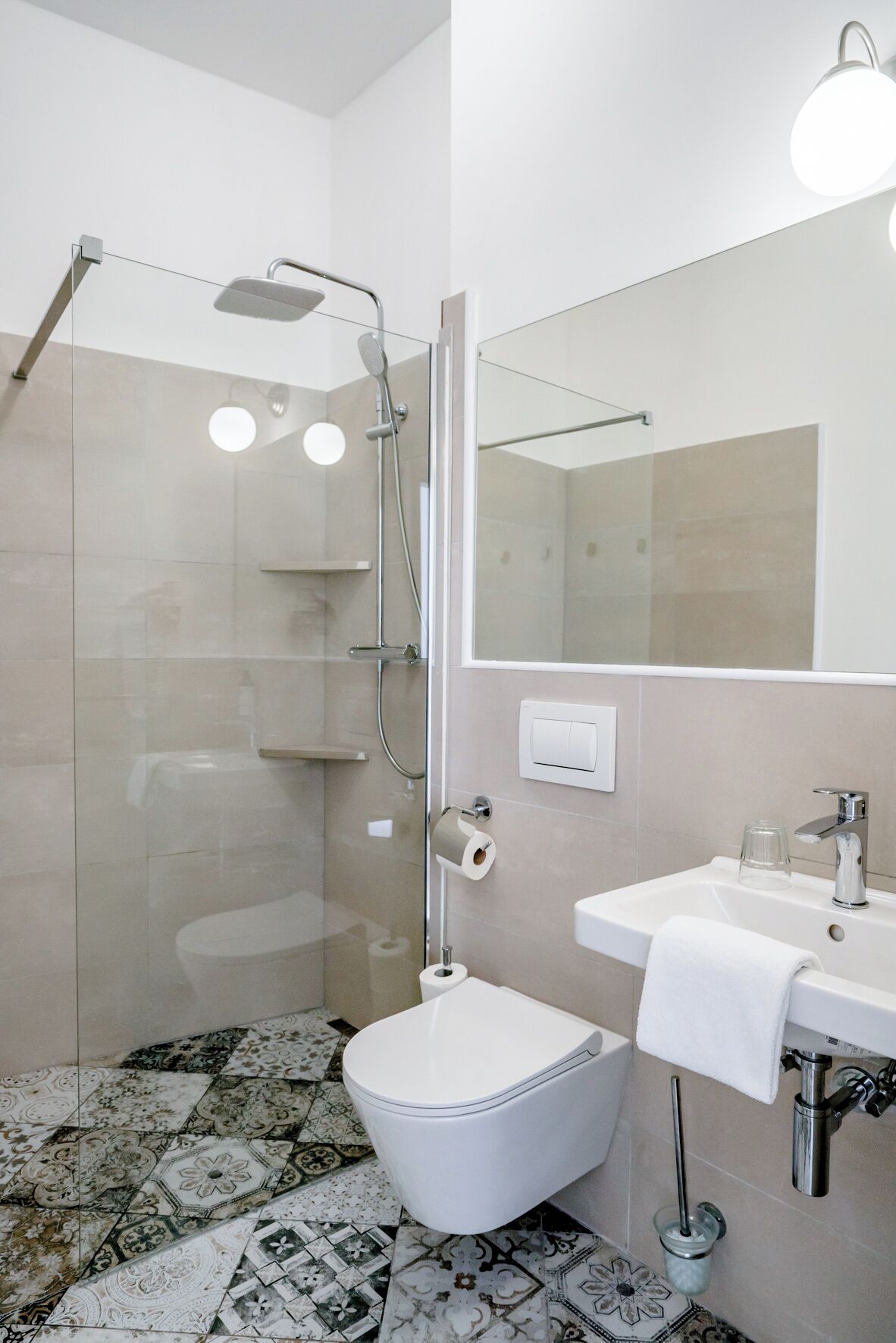 Un baño moderno con cabina de ducha de vidrio, inodoro blanco, lavamanos con espejo y baldosas de suelo estampadas.