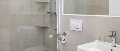 Un baño moderno con cabina de ducha de vidrio, inodoro blanco, lavamanos con espejo y baldosas de suelo estampadas.
