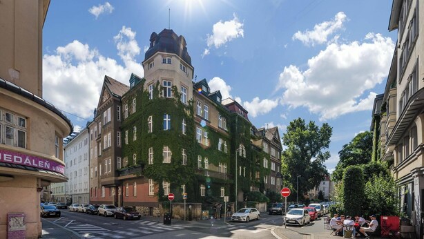 A corner building with a tower, ivy-covered walls, and a street with parked cars and pedestrians. - Elisabeth Old Town (Bratislava)