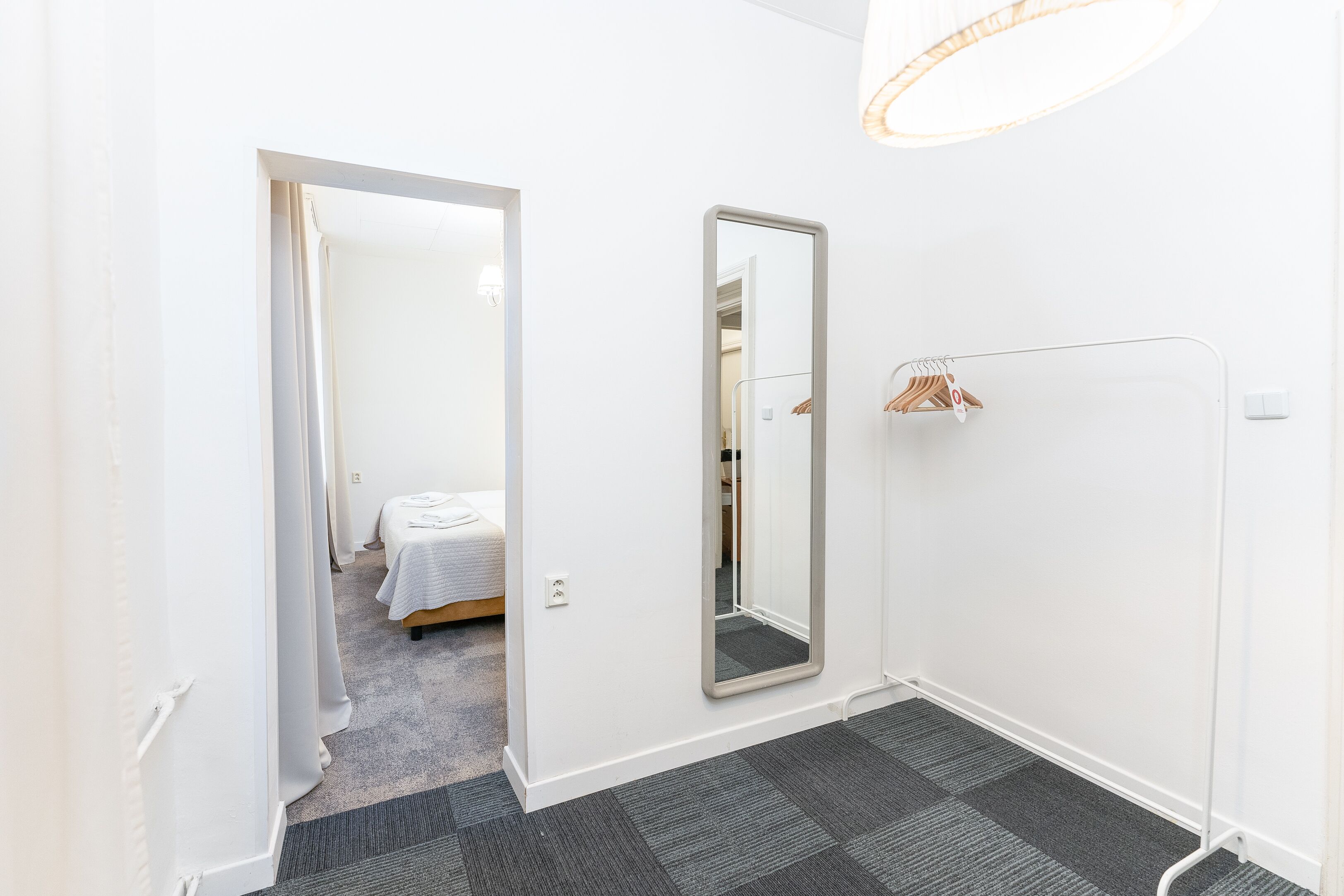 Ett hotellrum med en säng, en spegel, ett element och en klädstång.