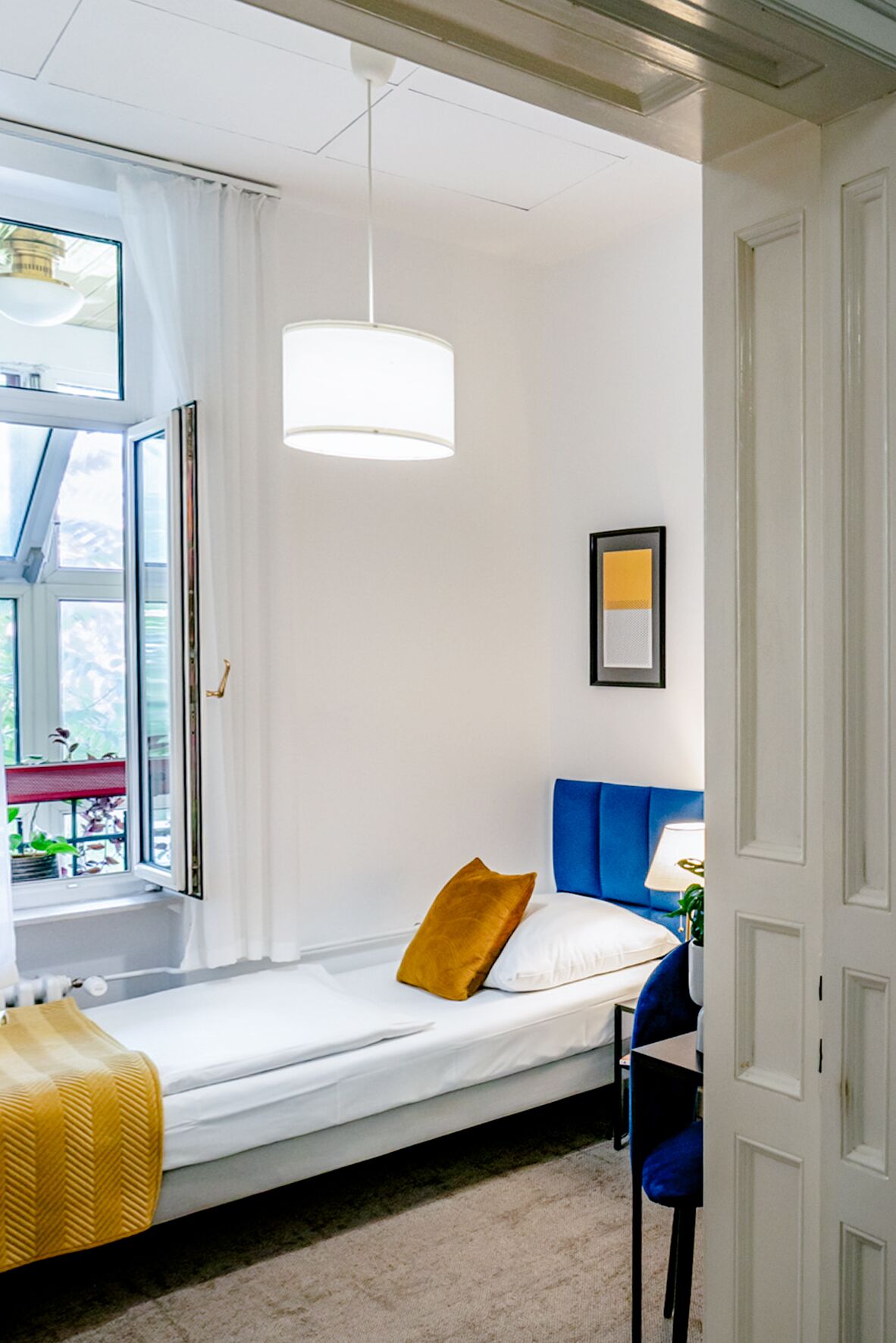 Habitació petita amb llit, finestra, llum penjant i porta.