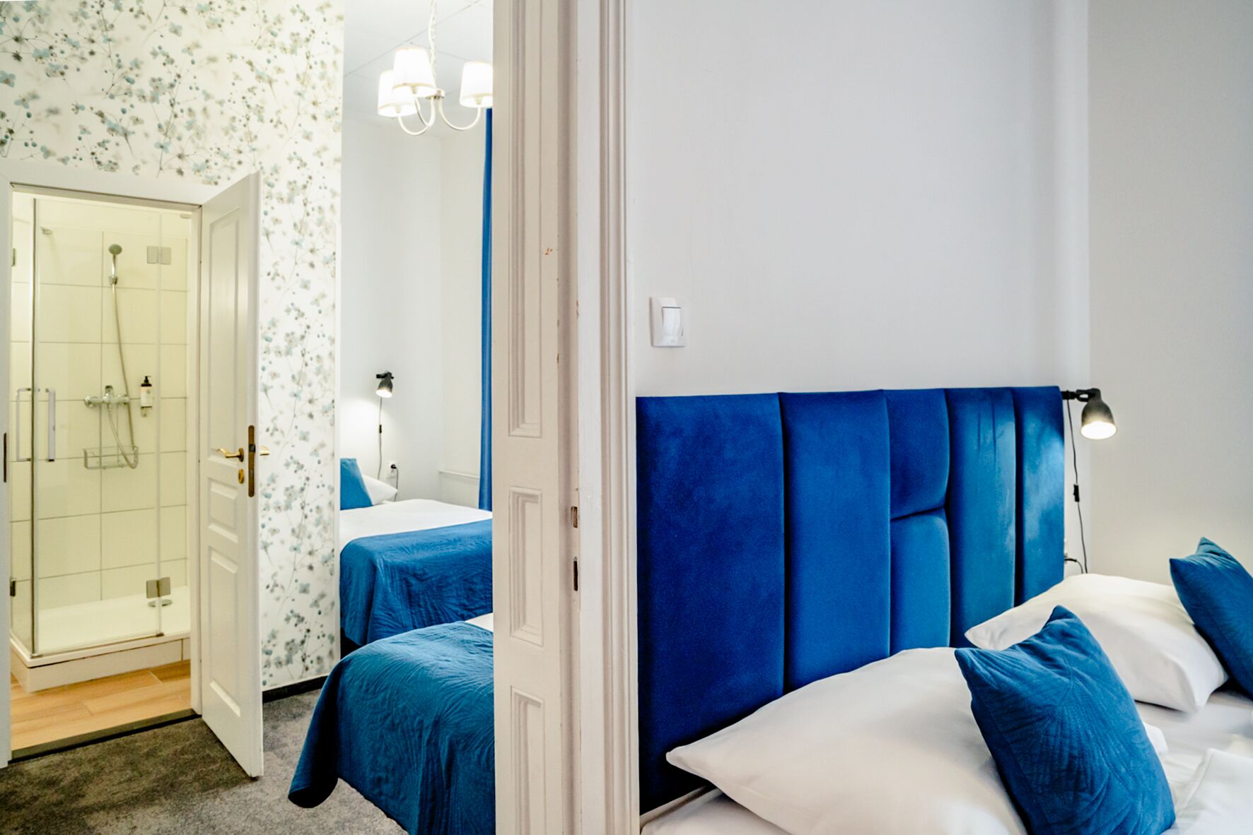 Habitación de hotel con ducha, cama con ropa de cama azul y cabecero blanco.