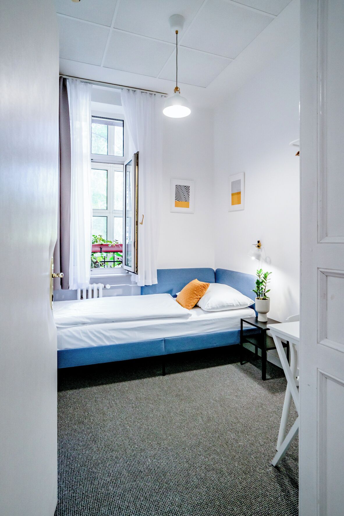 Um quarto com uma cama, uma mesinha de cabeceira com abajur, e duas molduras com quadros na parede.