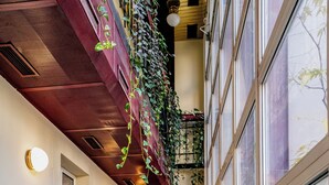 A narrow corridor with a wooden ceiling, a wall covered in green plants, and a large window on the right. - Elisabeth Old Town (Bratislava)
