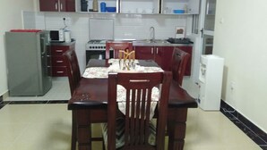 A compact kitchen with a dining table, chairs, a refrigerator, a stove, and cabinets. - S. Lucie Mango Apartment (Nairobi)