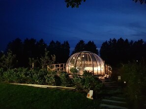 Eine große, kuppelförmige Gewächshauskonstruktion mit einer Holzterrasse davor.