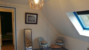 Ein Schlafzimmer mit schrägverdachter Decke, einem Dachfenster, einem Bett, einem Sessel, einem kleinen Tisch und einem Spiegel.