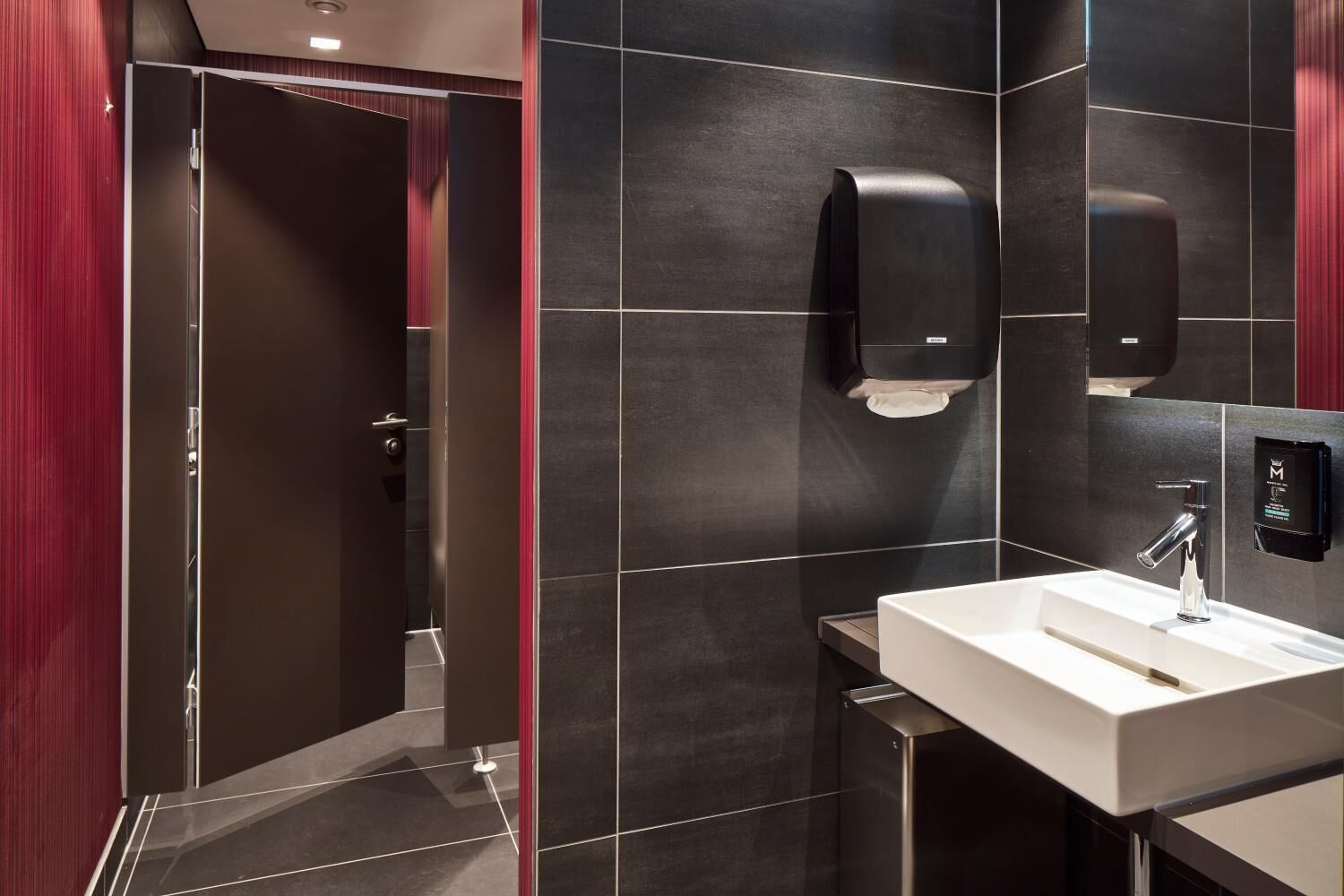 Un baño moderno con un lavamanos blanco, baldosas oscuras y una pared de acento roja.