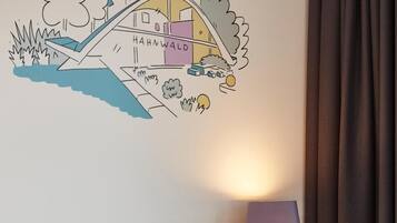 Ein Hotelzimmer mit einem Bett, weißen Kissen, einer Wandlampe und einer Wandsticker-Szene mit einer Brücke und Bäumen.
