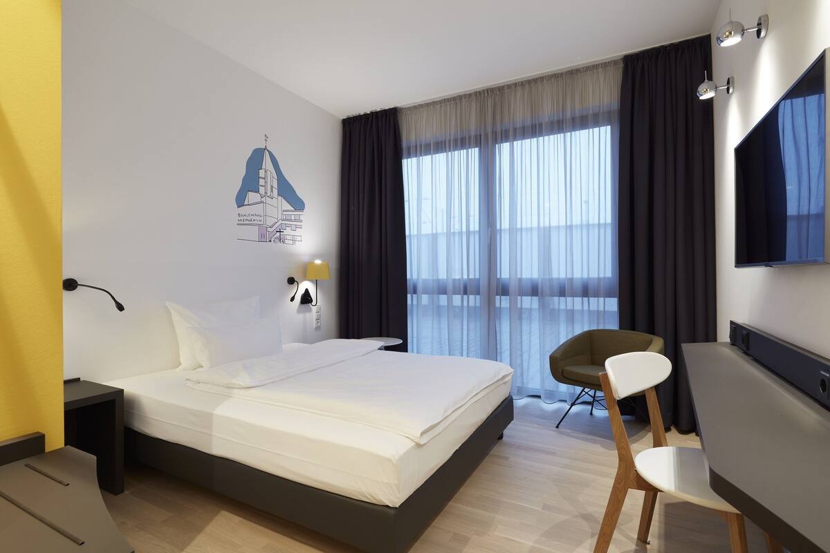 Een moderne hotelkamer met een groot bed, een bureau, een stoel, een televisie en een raam met gordijnen.