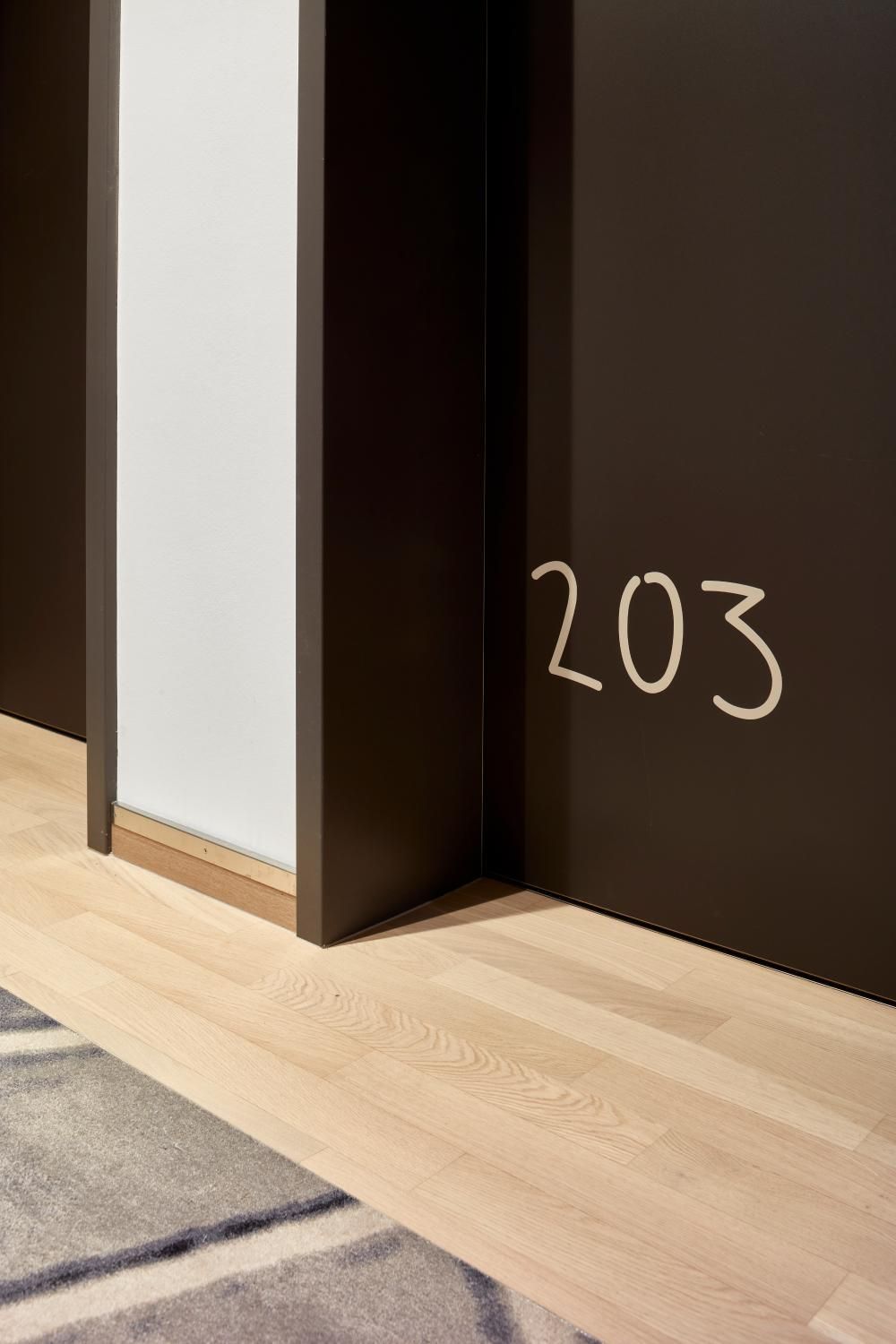Ein Korridor mit einer dunkelbraunen Wand und einer weißen Tür mit der Nummer 203.