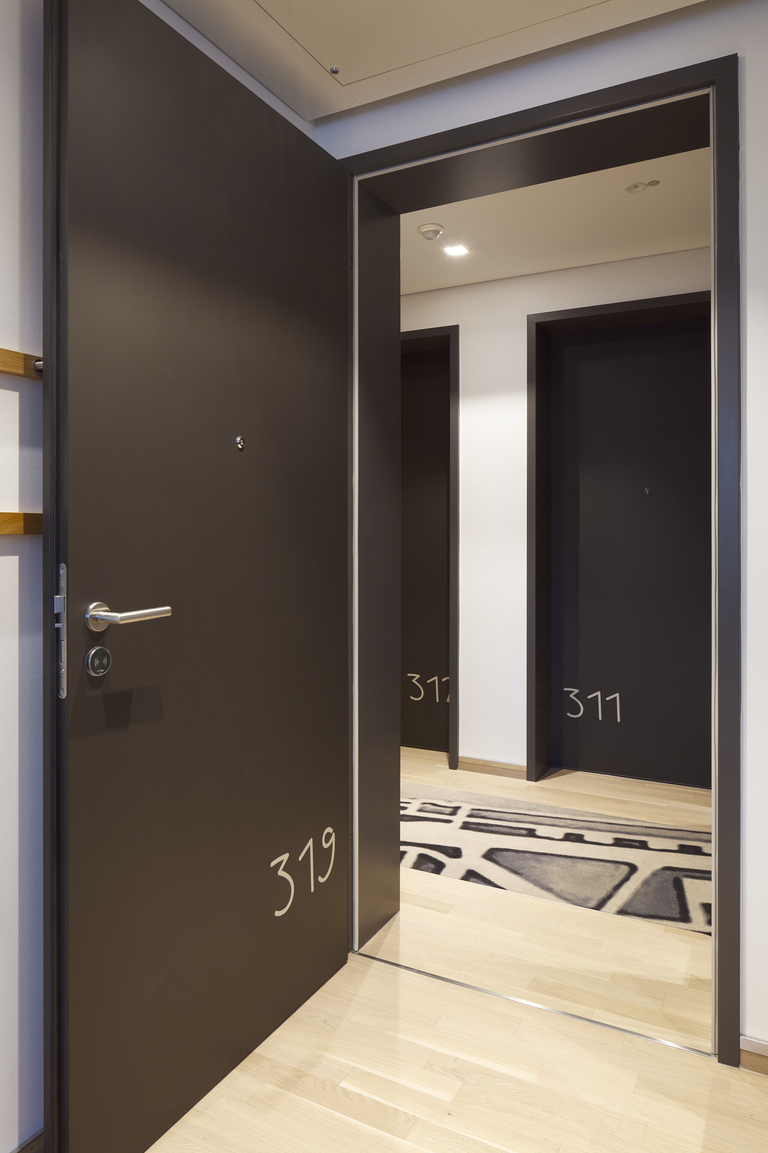 Ein Hotelzimmer mit einer dunklen Tür, einer sichtbaren Zimmernummer und einem gemusterten Boden.