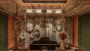 Una reception con pannello di legno, un cartello con su scritto "LES CABANES D'ELSA" e diversi elementi decorativi tra cui fiori e corone.