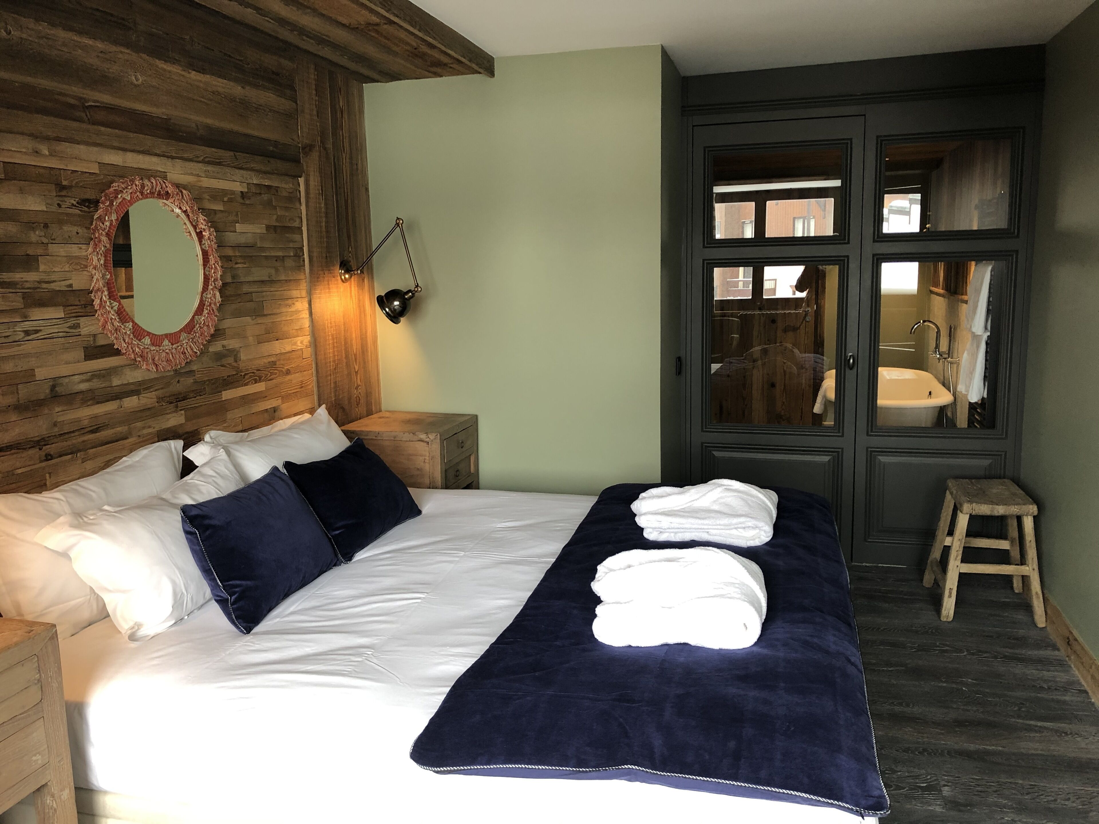 A neatly made bed with pillows, a bedside lamp, and a mirror on a wooden wall.