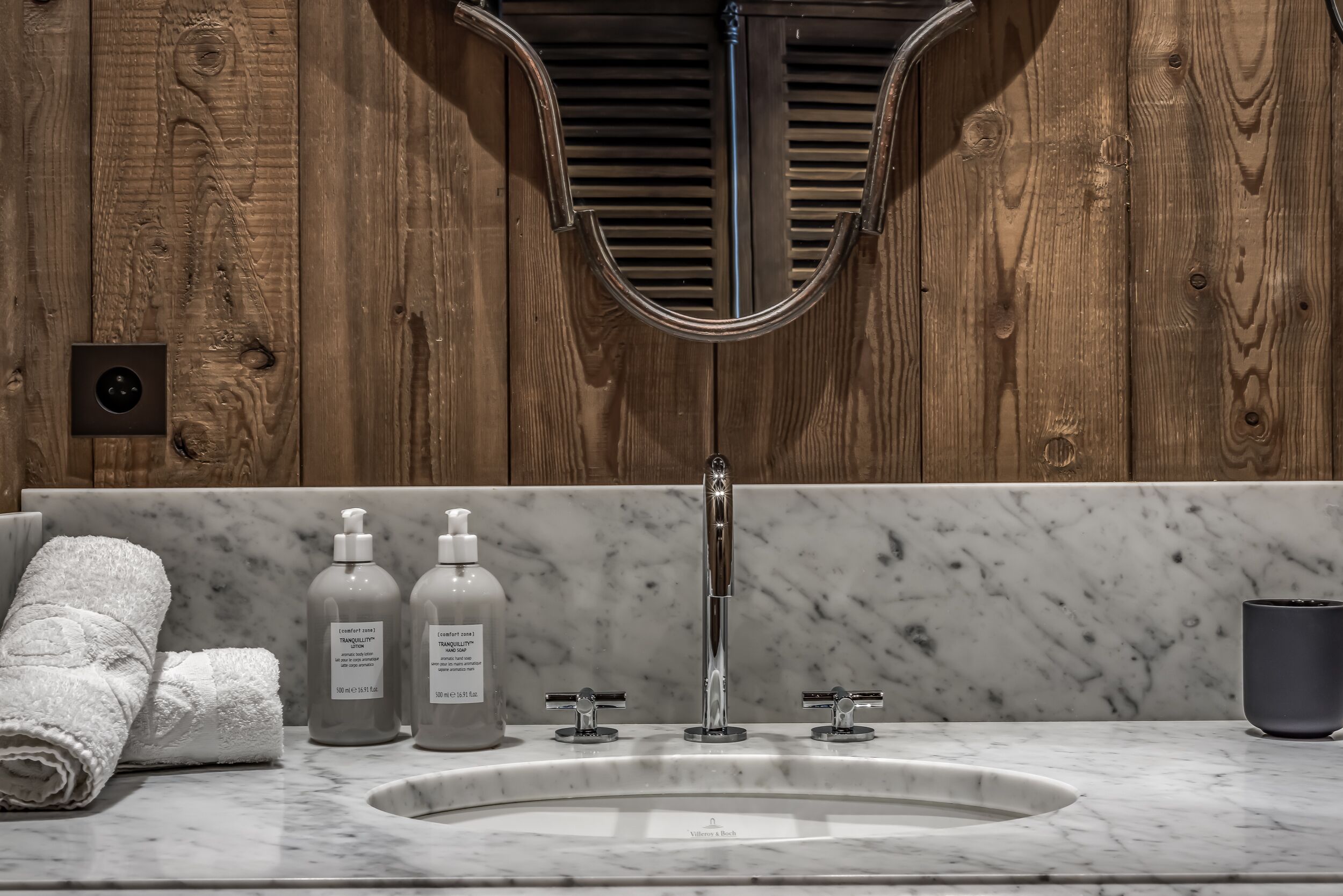 A bathroom with a wooden wall, a marble sink, and two soap dispensers.