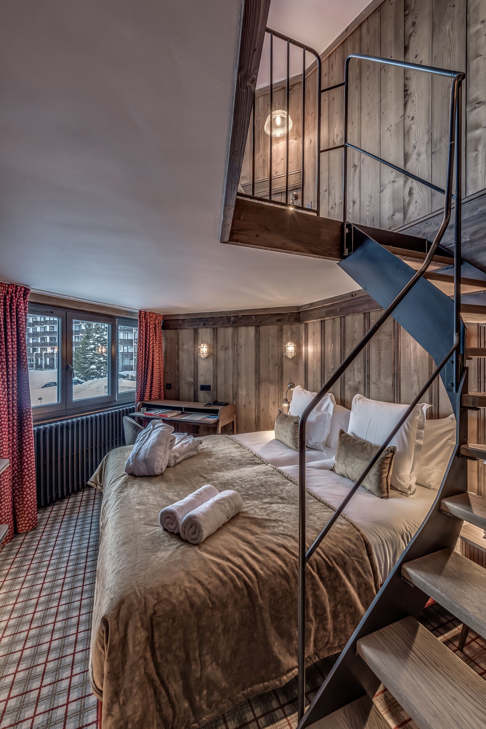 A bedroom with a large bed, a desk, and a spiral staircase.