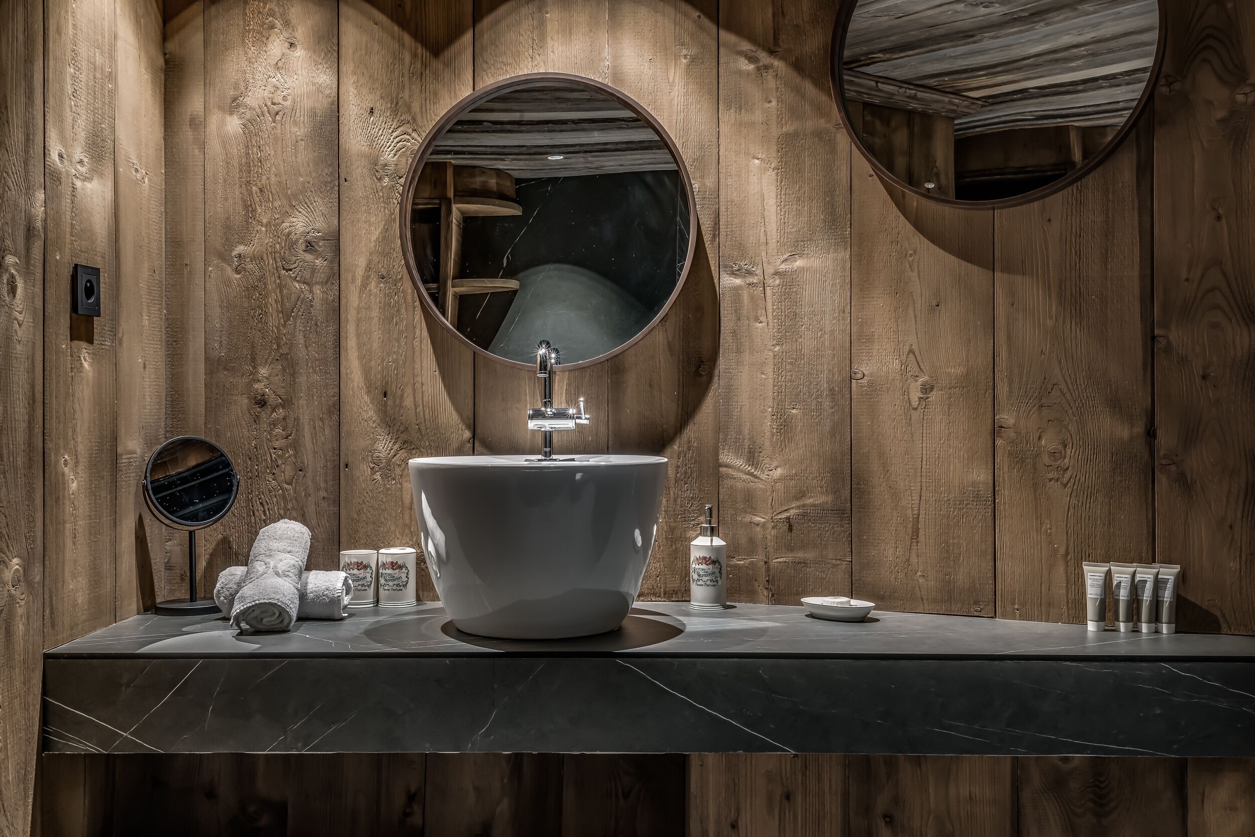 A bathroom with a large, round mirror, a white sink, and wooden paneling.