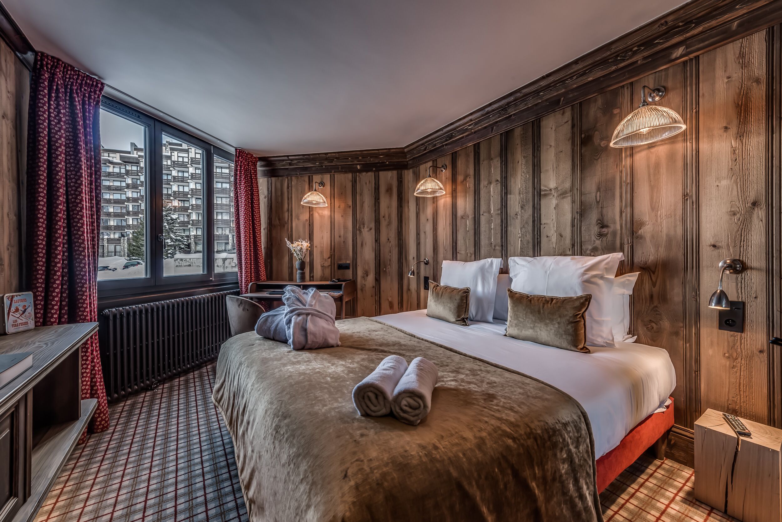 Un dormitorio con una cama grande, paredes de madera y vistas a edificios.