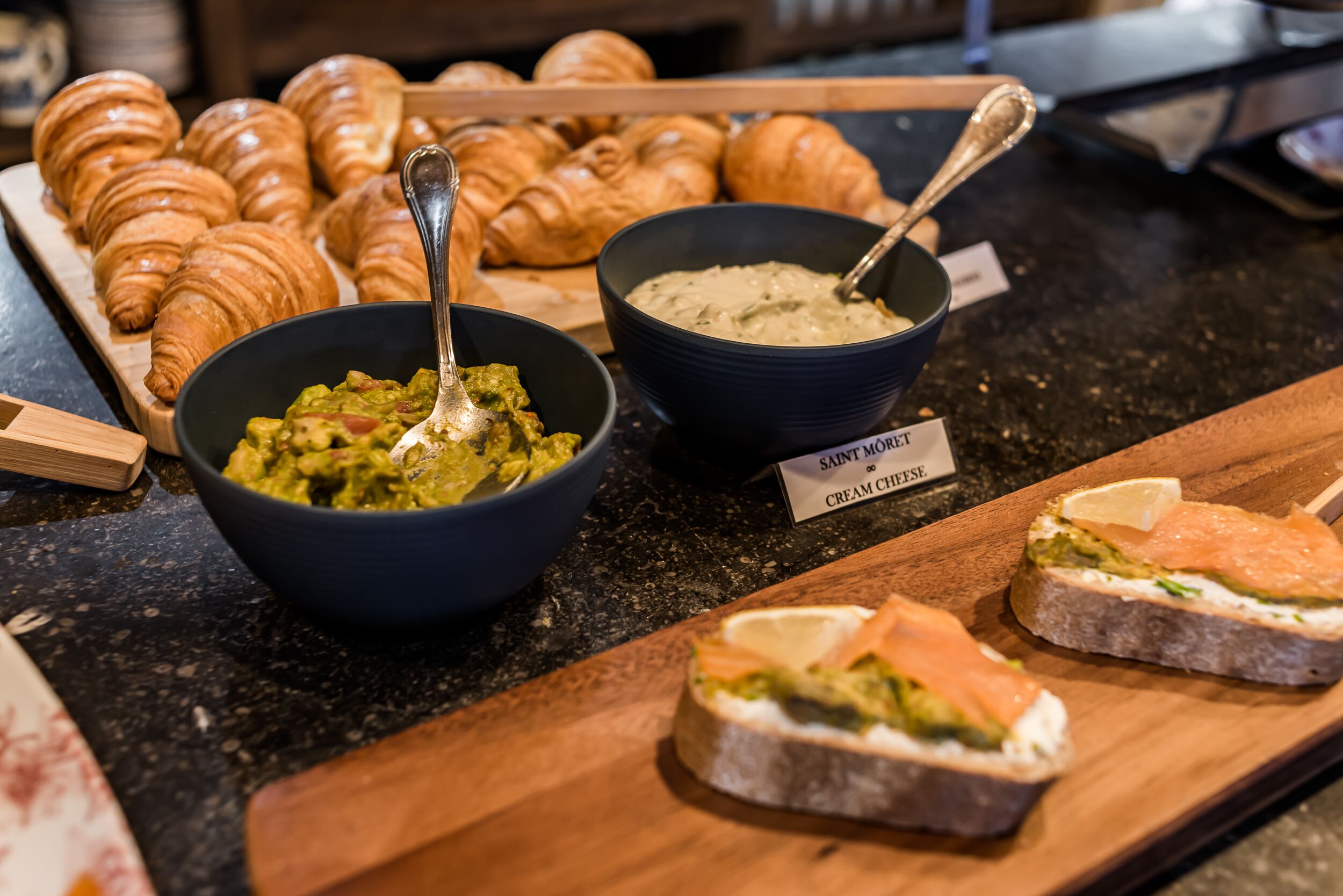 En buffé med croissanter, skålar med guacamole och färskost samt smörgåsar.