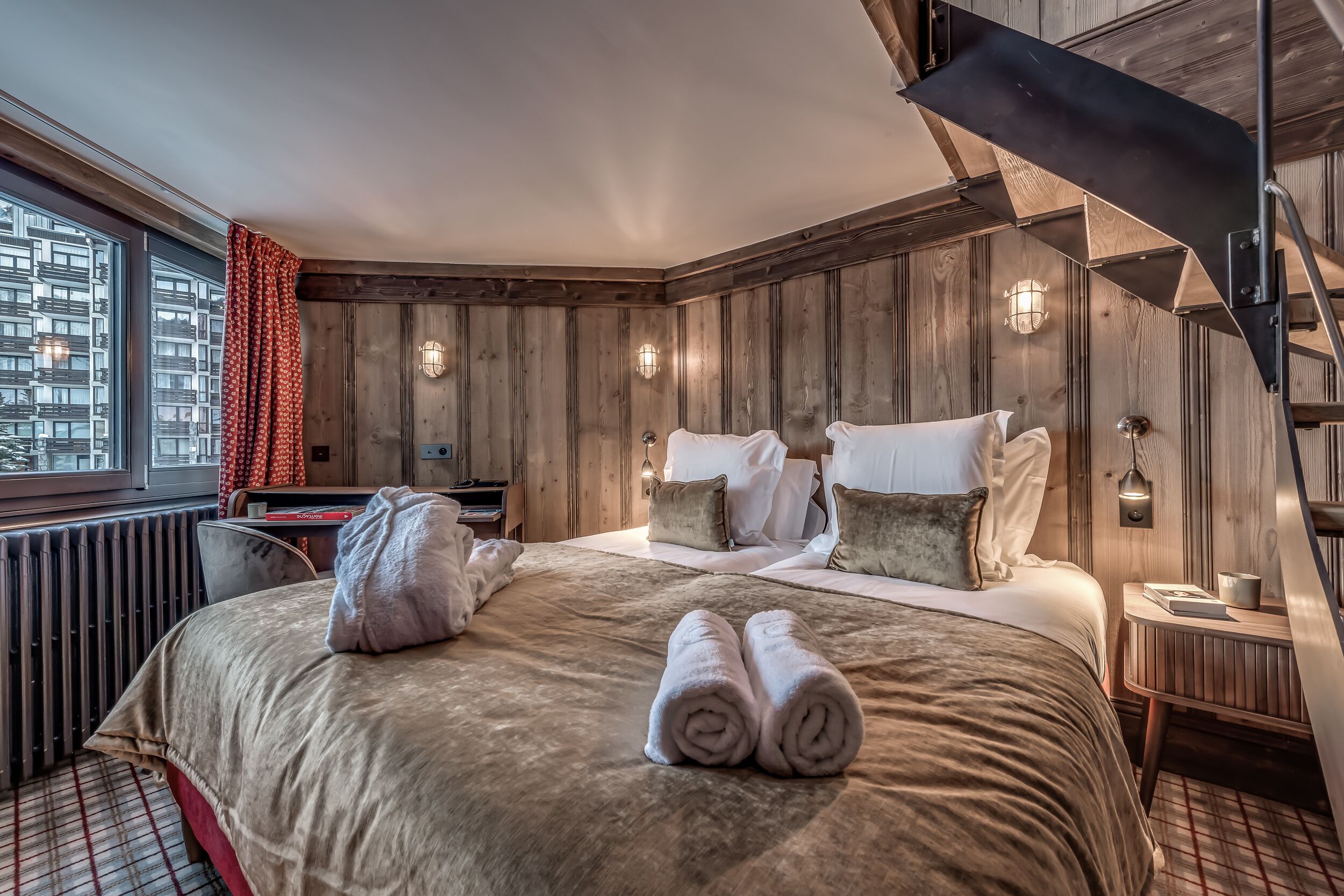 Camera d'albergo con un letto grande, pannelli in legno, una scrivania e una finestra con tende.