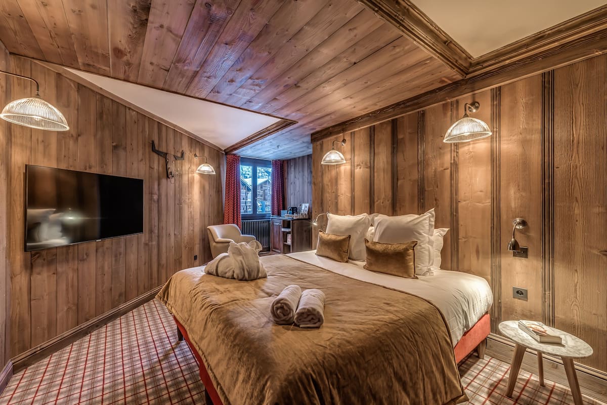 A wooden-paneled bedroom with a large bed, a flat-screen TV, and a small table.