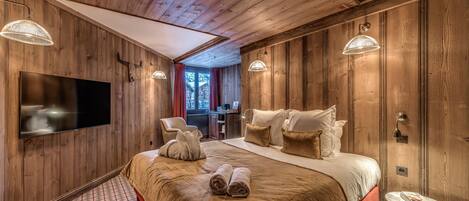A wooden-paneled bedroom with a large bed, a flat-screen TV, and a small table.